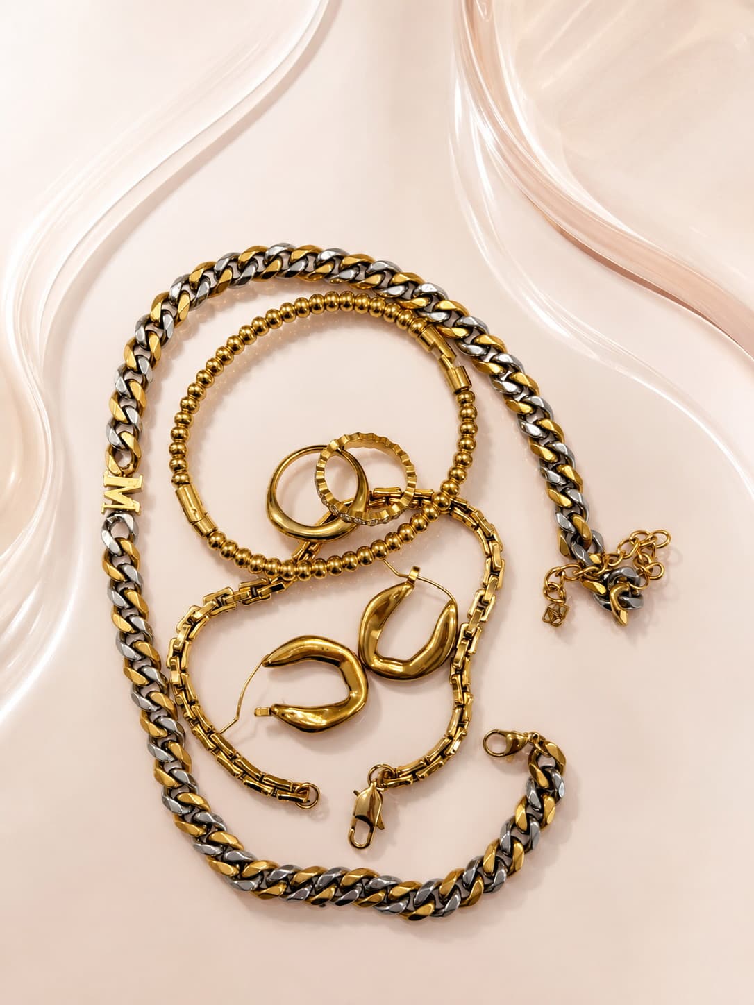 Gold chain necklaces, hoop earrings and rings arranged on a pale surface