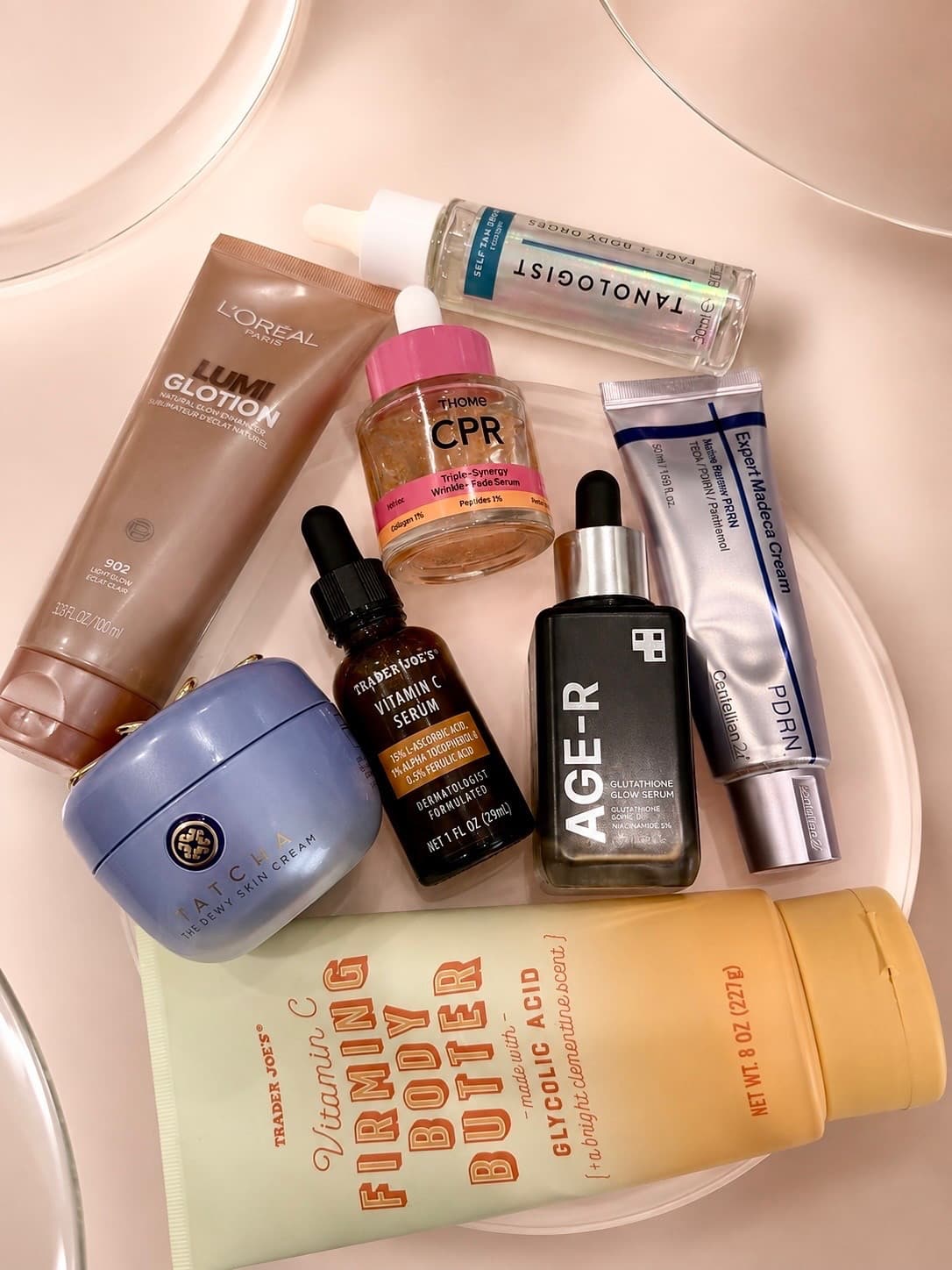 A flat lay of skincare and body products including serums, body butter and tanning drops
